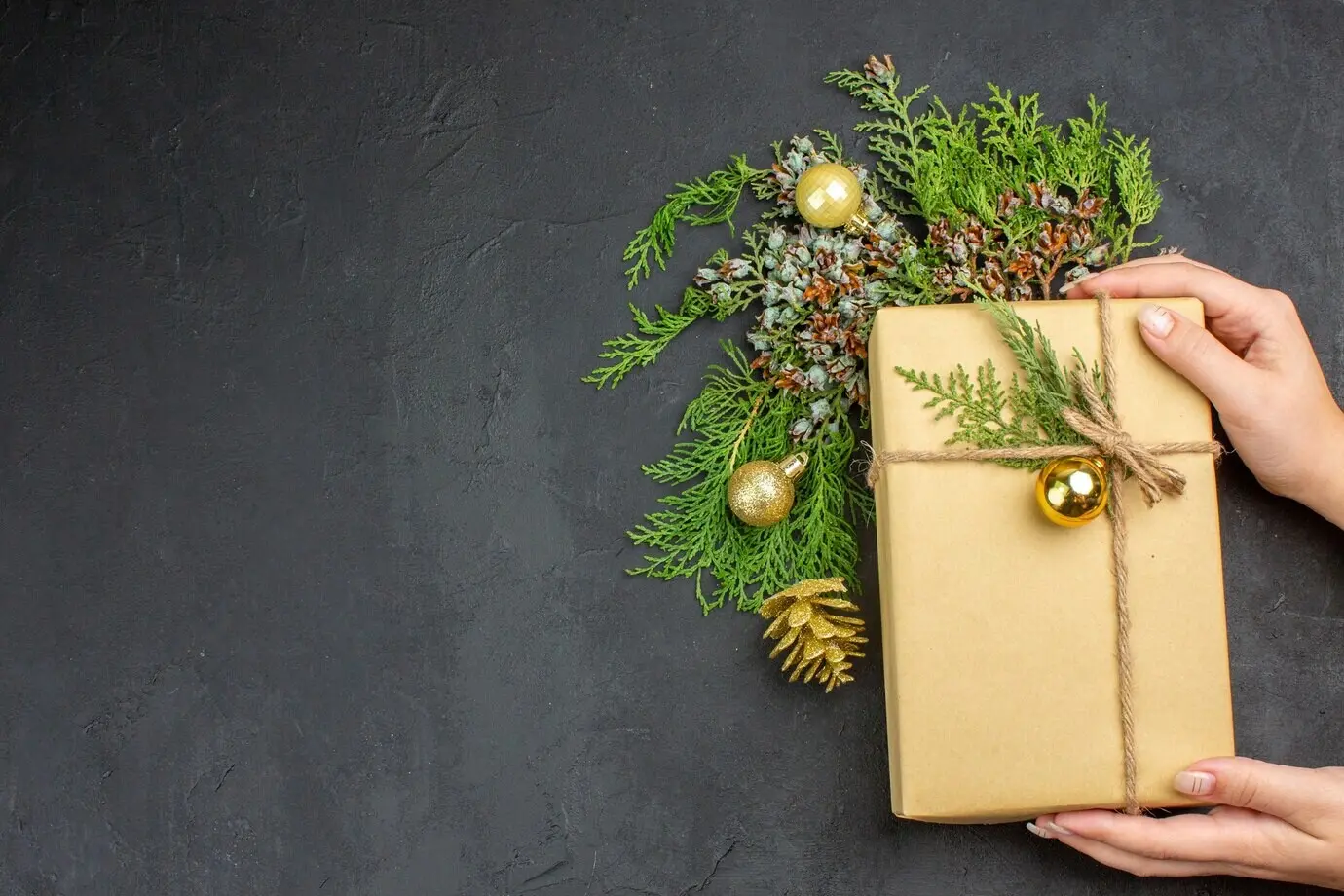 Ansicht von oben: Weihnachtsgeschenk, Tannenzweige und Christbaumschmuck auf beiger Oberfläche.